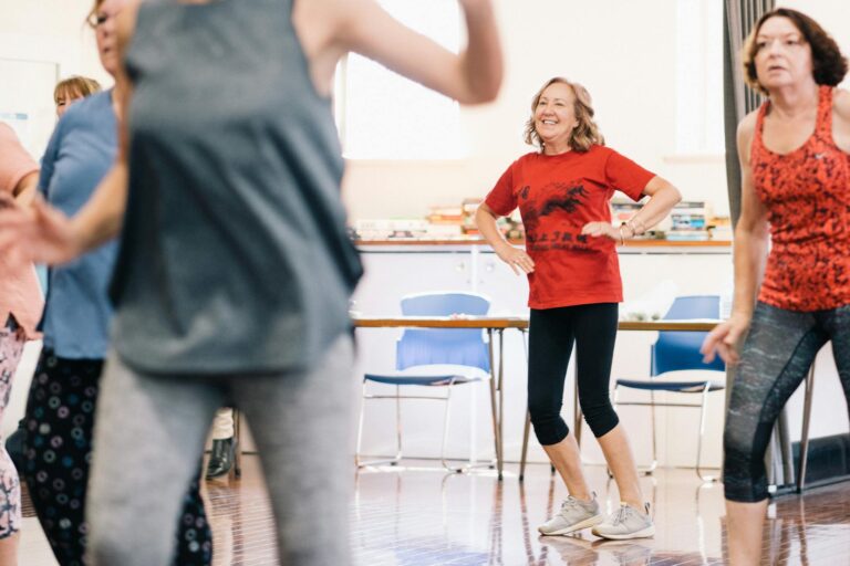 A vibrant dance class indoors with smiling women, encouraging a healthy lifestyle.